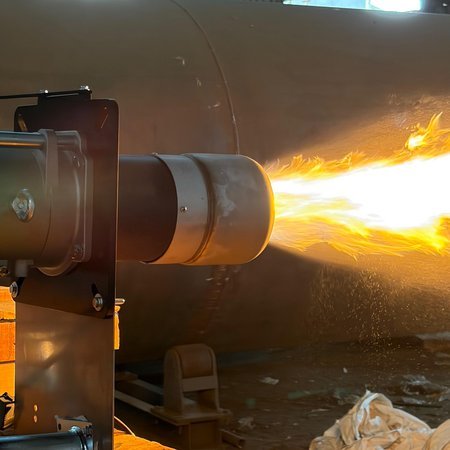 Close-up of a burner firing a live test flame against a boiler shell in the workshop