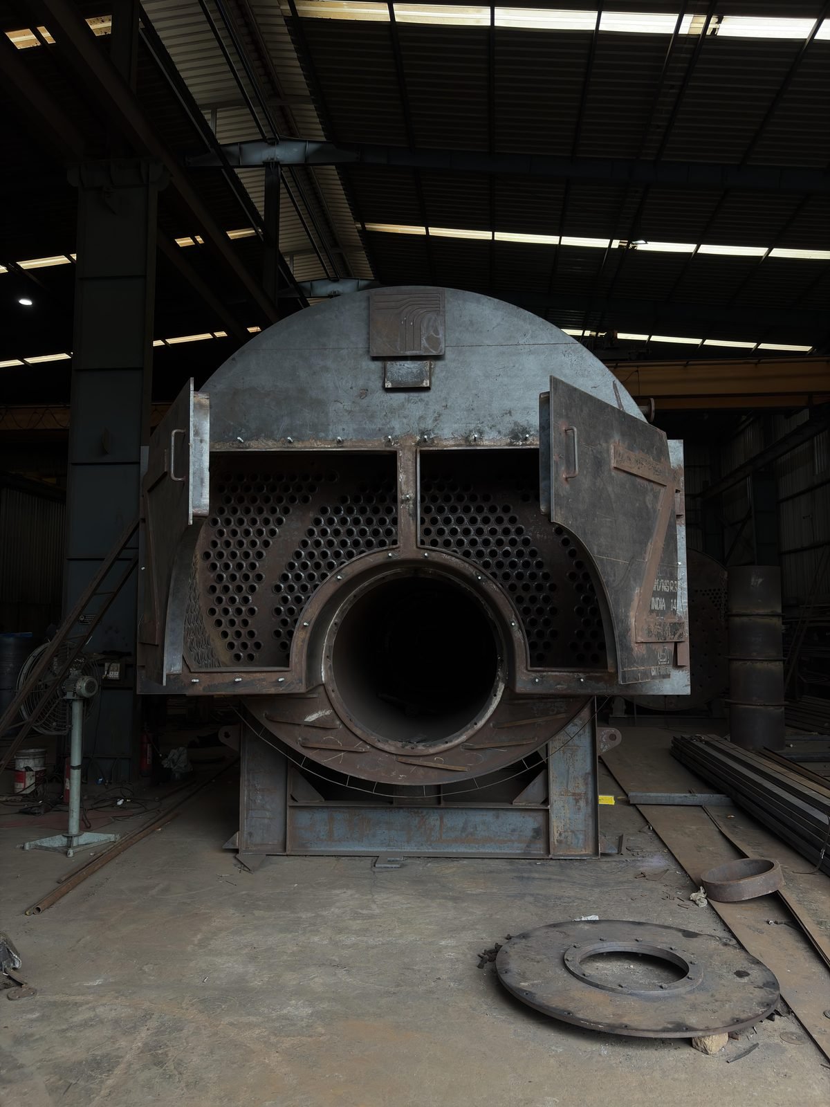 A three-pass steam boiler shell under fabrication on the Dhamatwan shop floor, tube nest and access doors visible